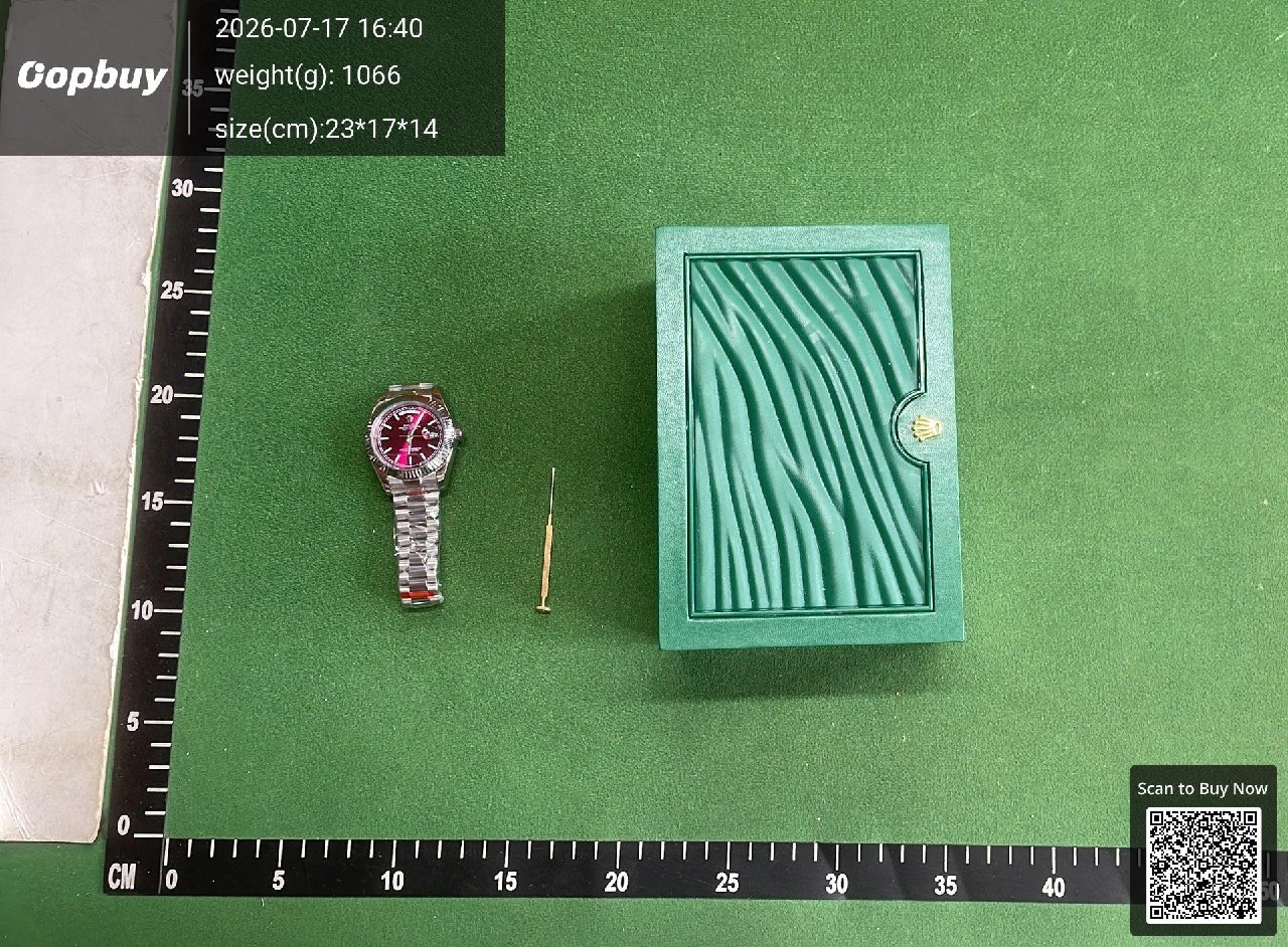 The same watch on the measuring mat beside a green presentation box and a small thin tool